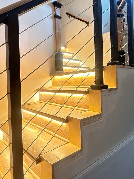 Modern staircase with glowing LED step lights and black cable railing in a home interior