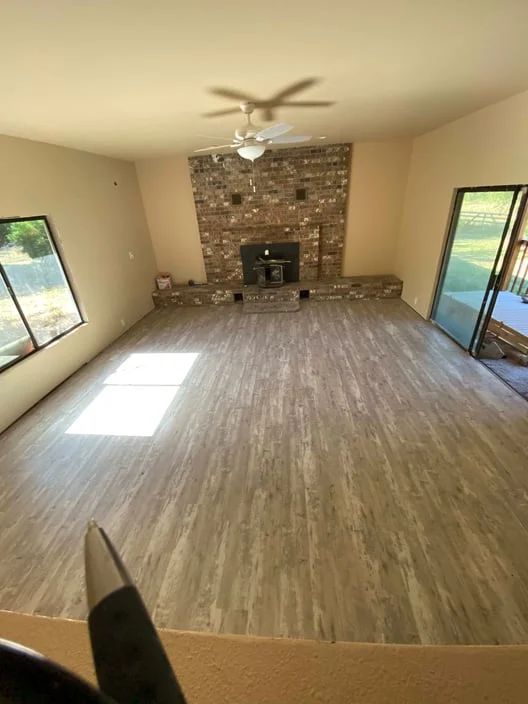 Empty living room with wood floors, brick fireplace, ceiling fan, and sliding glass doors on both sides