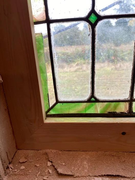 Stained-glass window with a green accent, showing an outdoor view above a cracked windowsill.