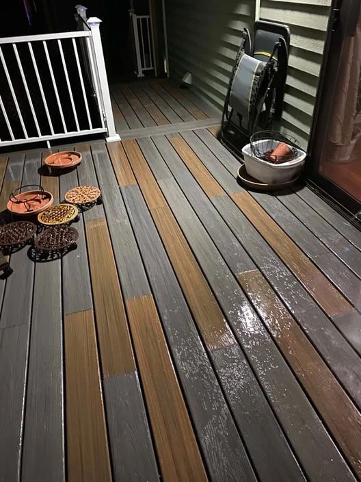Front porch with gray and brown deck boards, potted plants, and a railing at night.