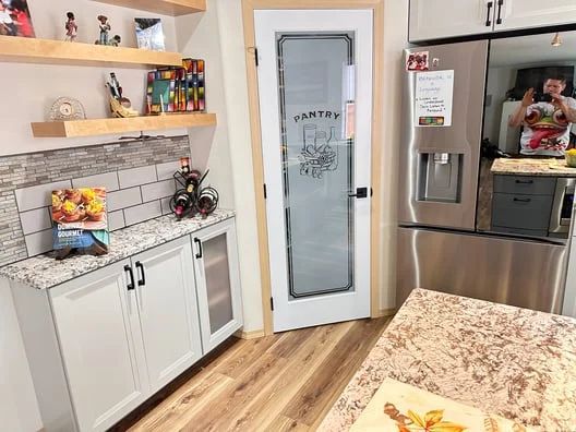 Modern kitchen with island, two black stools, white cabinets, stainless appliances, and subway tile backsplash