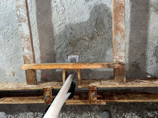 Wooden bench and concrete wall with a white pipe running through an opening