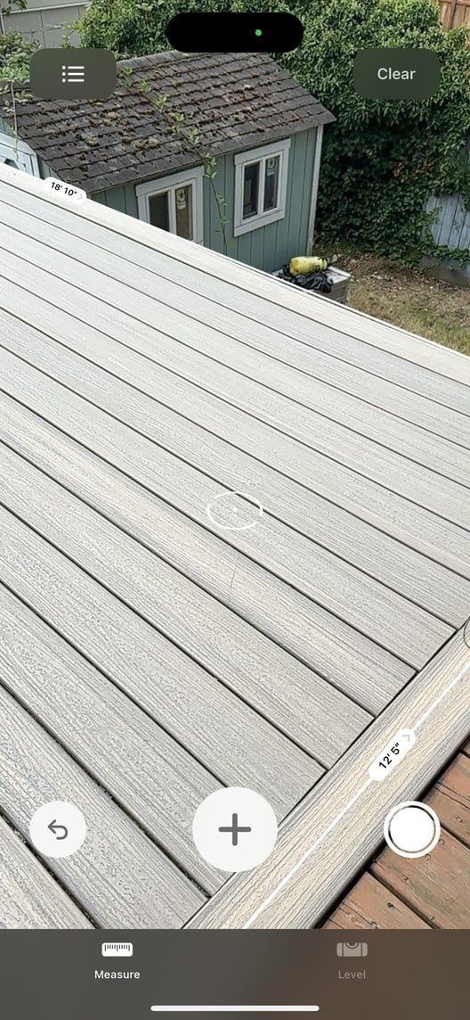Rooftop view of light gray shingles overlooking a small gray house and trees below.
