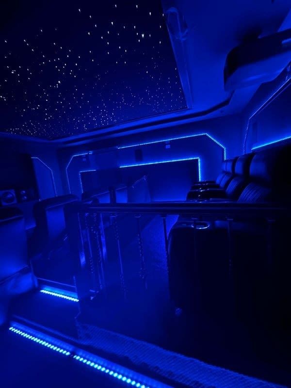 Blue-lit luxury bus interior with starry ceiling lights and empty seats