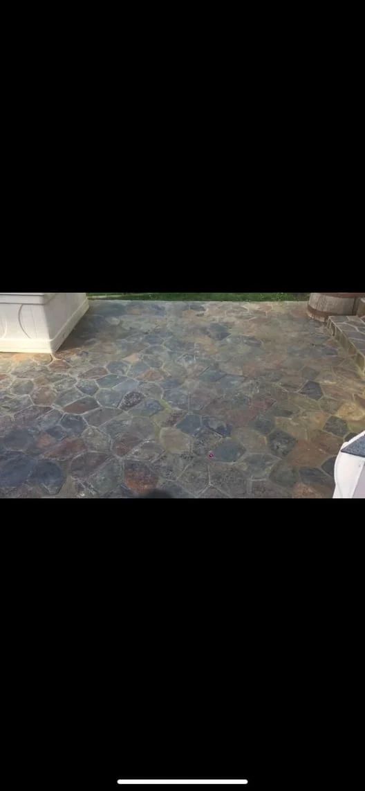 Stone-tiled patio with mottled gray and blue flooring, bordered by light walls and a small step.