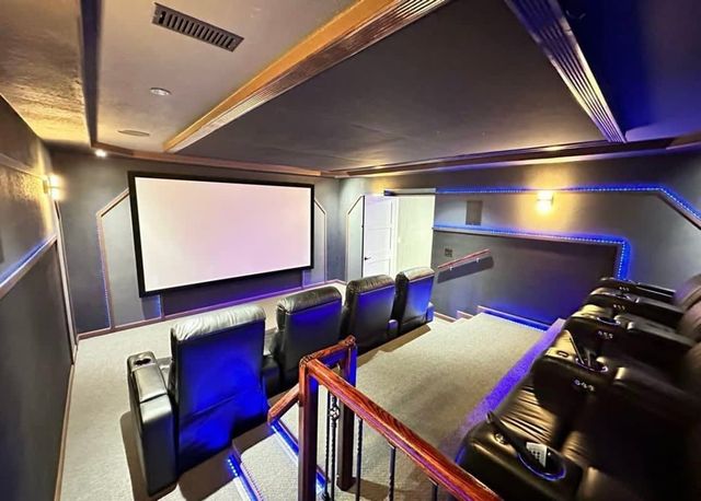 Modern home theater with projector screen, blue accent lighting, and rows of black recliner seats
