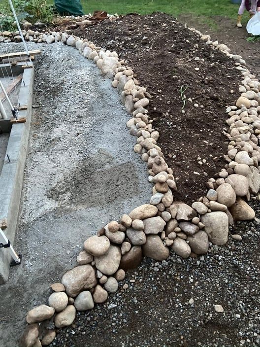 Stone-bordered garden bed beside a gravel path and concrete walkway under construction
