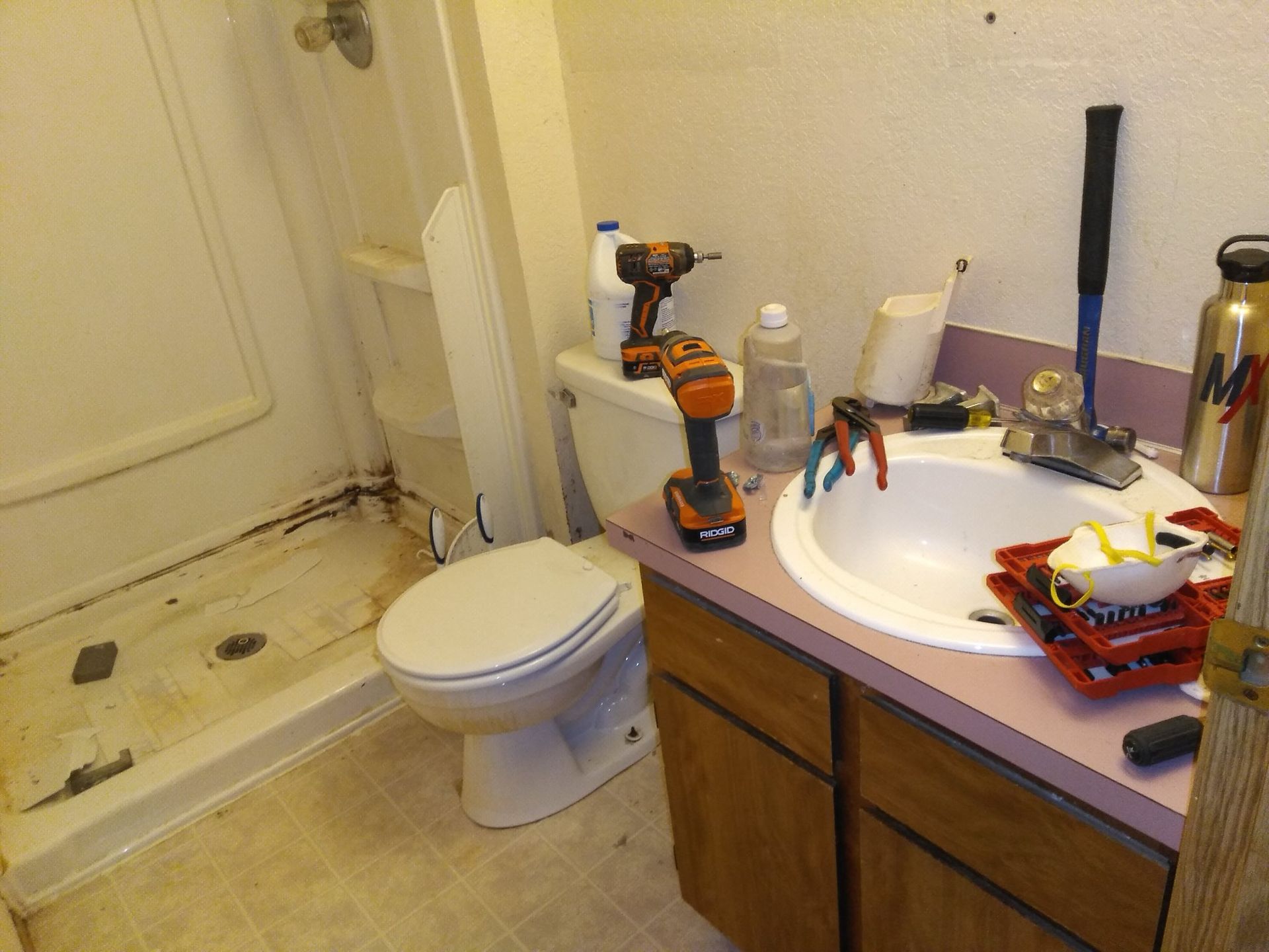 Cluttered bathroom with toilet, sink, tools, and scattered items on the counter and floor
