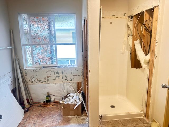 Small bathroom under renovation with exposed wall studs, shower stall, and debris on the floor