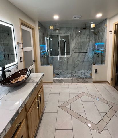 Small bathroom with tiled walk-in shower, toilet, and sink with a toilet-seat elevator assist device