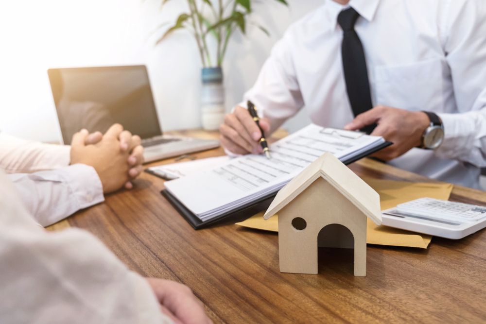 Person Signing Paperwork at a Desk With a Small House Model — Linda Emery & Associates In Gosford, NSW