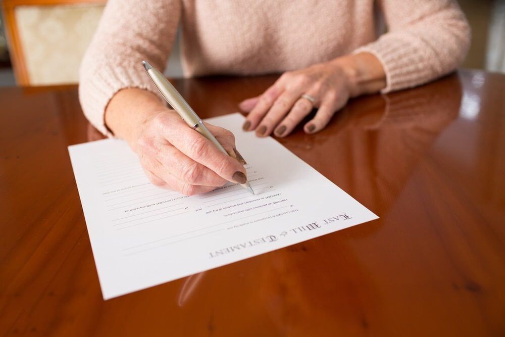 A Woman Is Sitting at A Table Writing on A Piece of Paper with A Pen — Linda Emery & Associates In Gosford, NSW