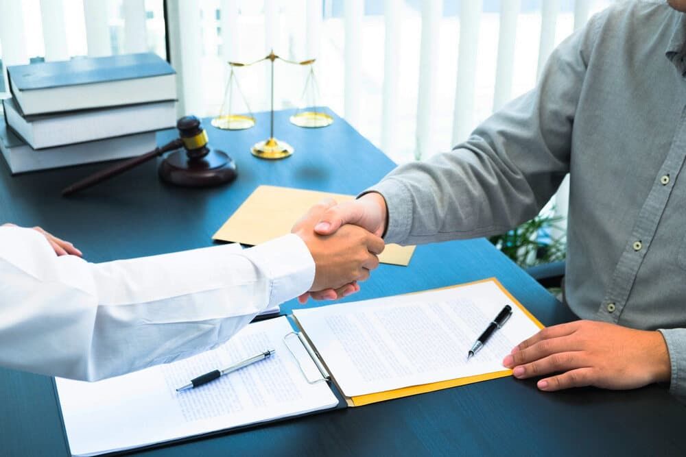 A Man Is Shaking Hands with Another Man While Sitting at A Desk — Linda Emery & Associates In Gosford, NSW