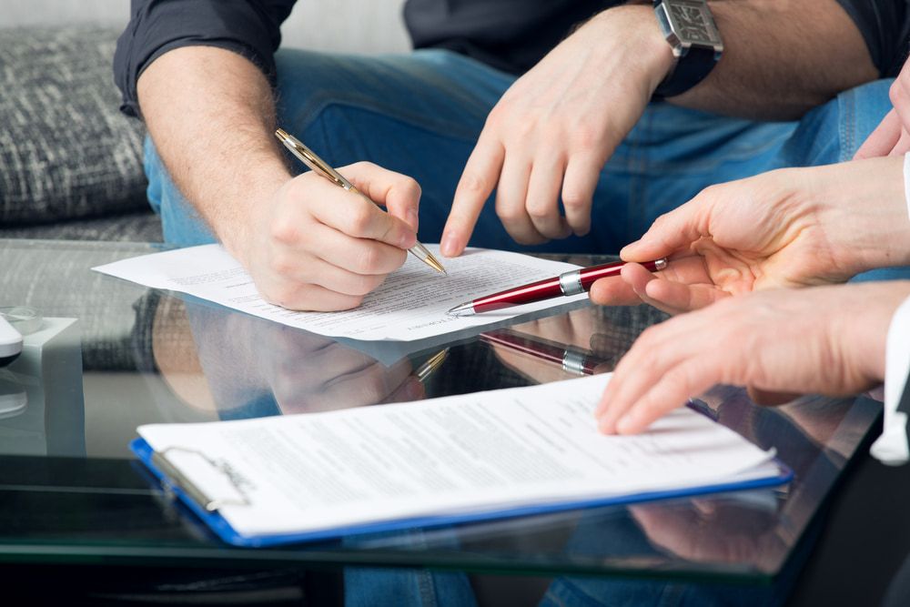 A Group of People Are Sitting at A Table Signing a Document — Linda Emery & Associates In Gosford, NSW