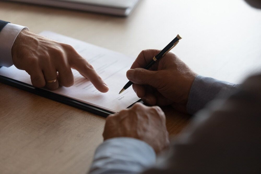 A Man Is Signing a Document While Another Man Points at It — Linda Emery & Associates In Gosford, NSW