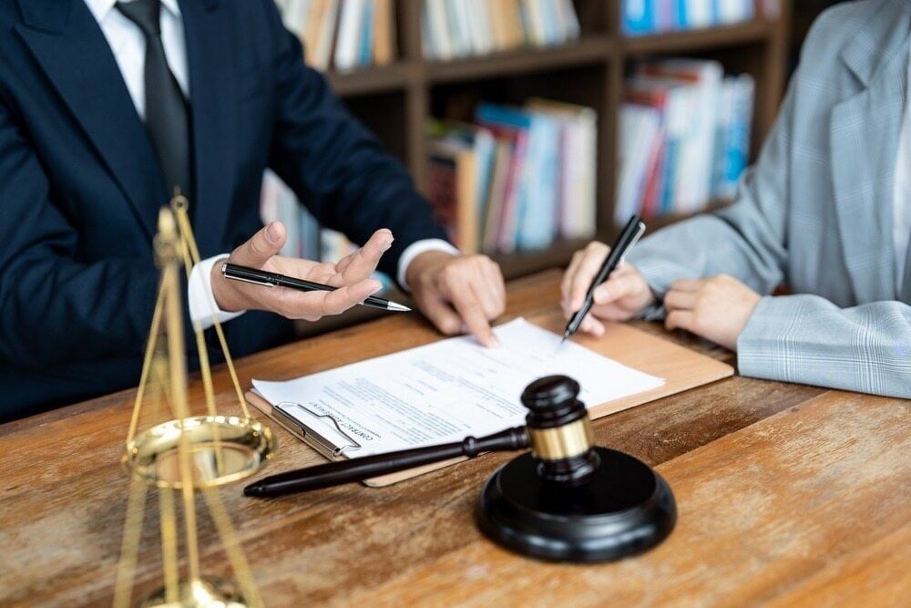 A Man and A Woman Are Sitting at A Table Signing a Document — Linda Emery & Associates In Gosford, NSW