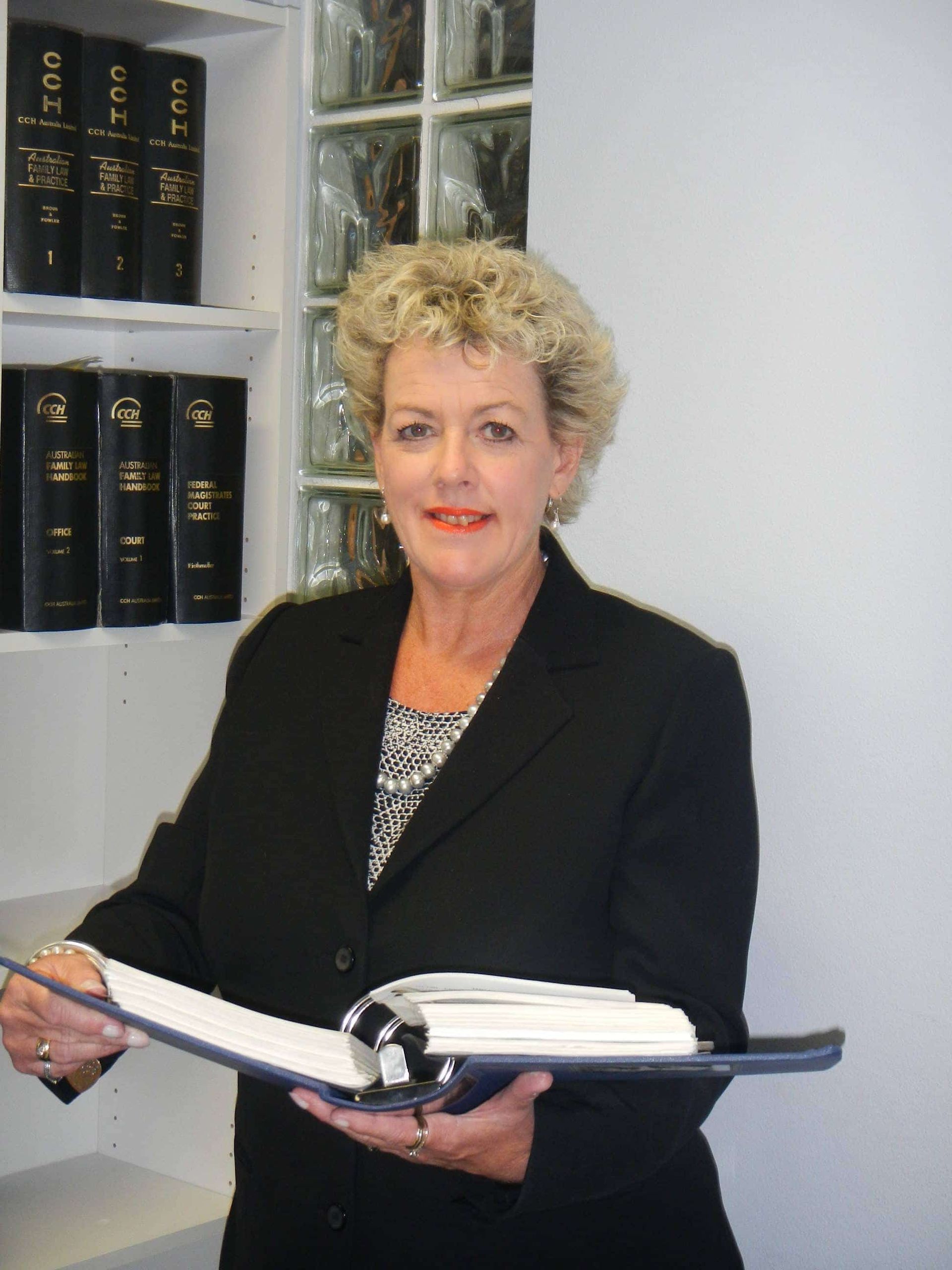 A woman in a black suit is holding a binder in her hands — Linda Emery & Associates In Gosford, NSW