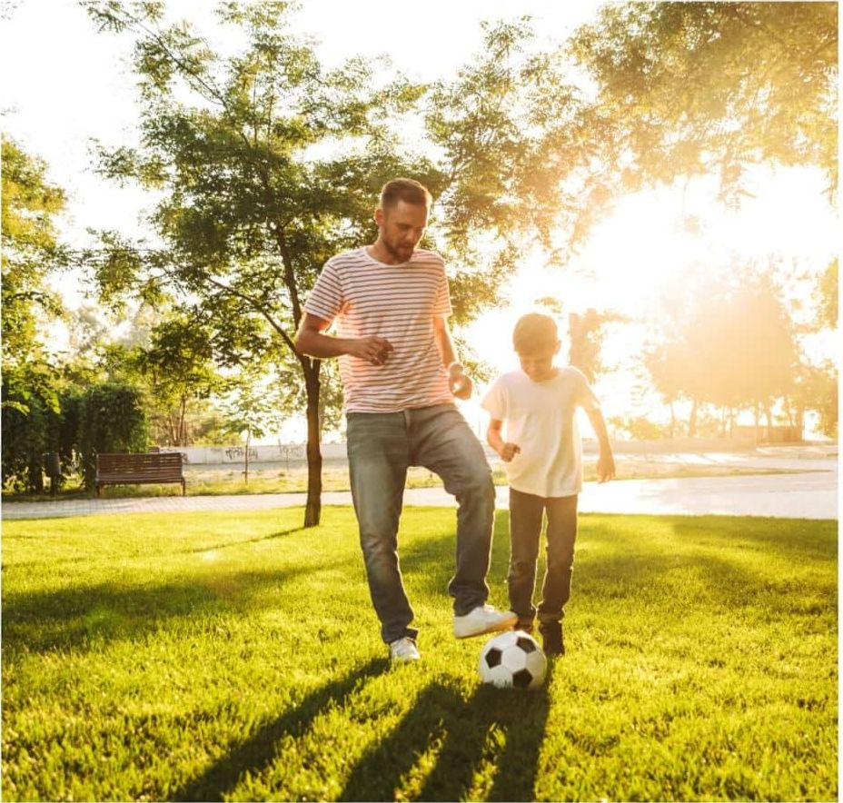A Man and A Boy Are Playing Soccer in A Park — Linda Emery & Associates In Gosford, NSW