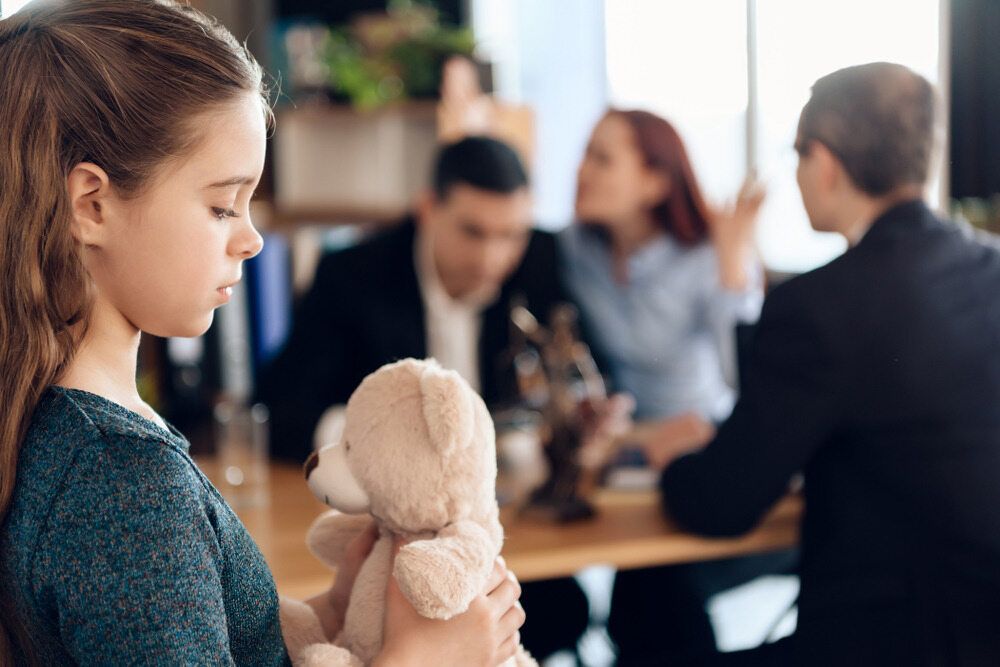 A Little Girl Is Holding a Teddy Bear in Front of A Family — Linda Emery & Associates In Gosford, NSW