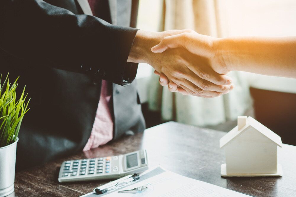 A Man in A Suit and Tie Is Shaking Hands with A Woman in Front of A Model House — Linda Emery & Associates In Gosford, NSW