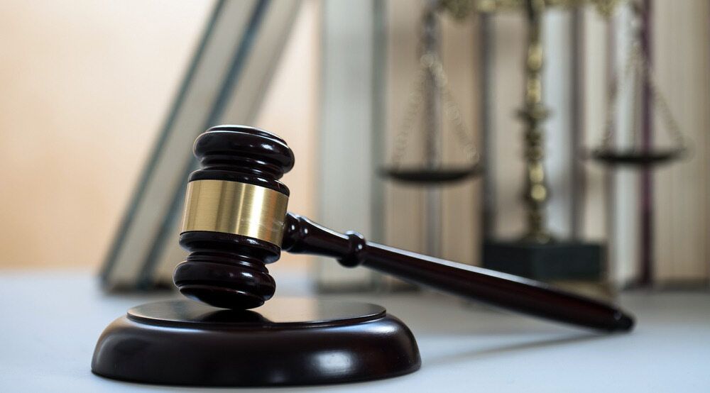 A Wooden Judge 's Gavel Is Sitting on A Table in Front of A Scale of Justice — Linda Emery & Associates In Terrigal, NSW