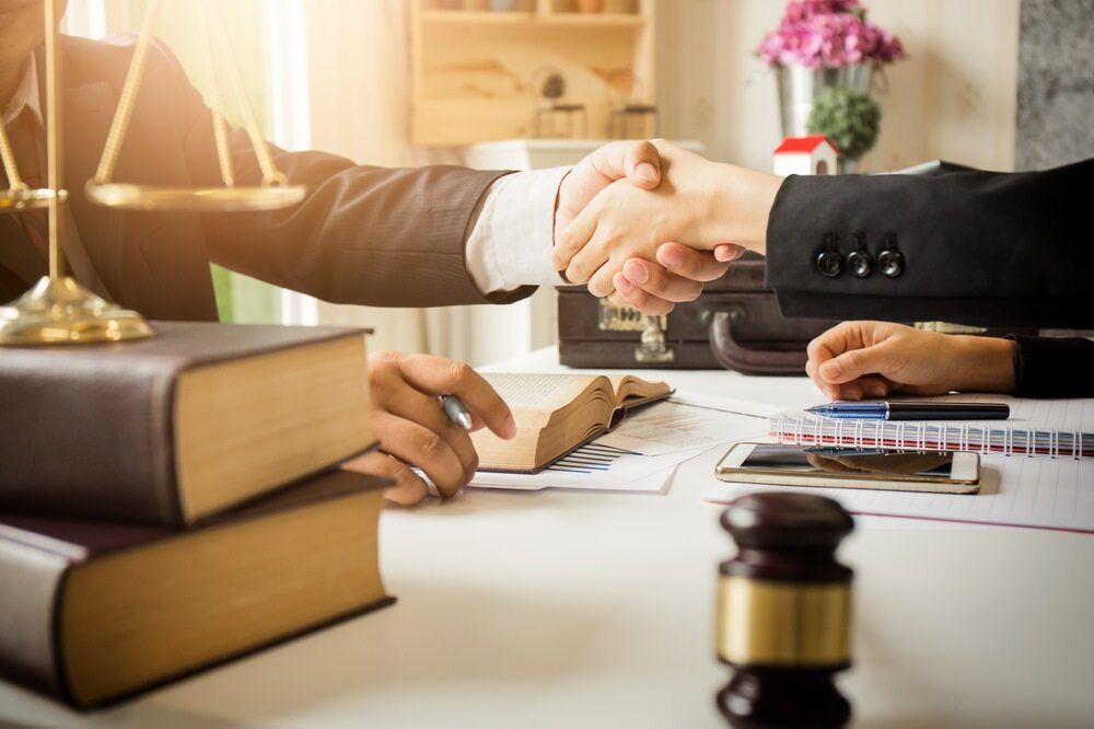 A Lawyer Is Shaking Hands with A Client While Sitting at A Desk — Linda Emery & Associates In Gosford, NSW