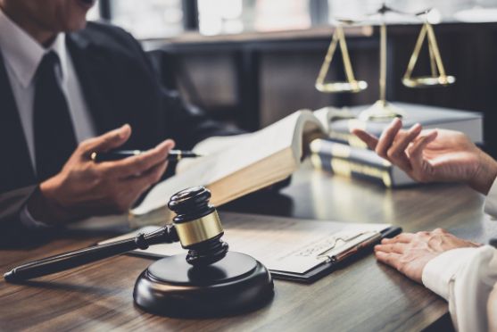 A Man and A Woman Are Sitting at A Table with A Gavel and Scales of Justice — Linda Emery & Associates In Wyong, NSW