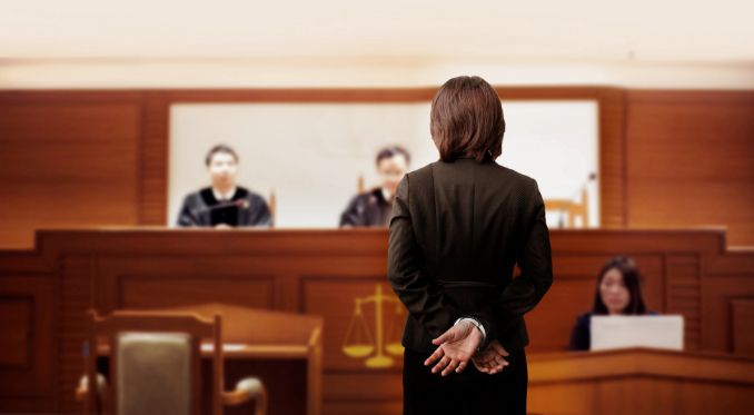 A Woman Is Standing in Front of A Judge in A Courtroom — Linda Emery & Associates In Morisset, NSW