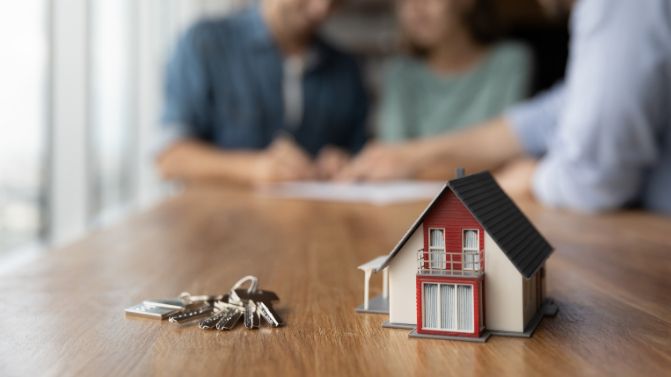 A Couple Is Sitting at A Table with A Model House and Keys — Linda Emery & Associates In Tuggerah, NSW