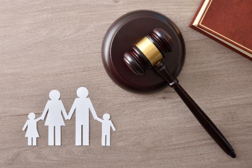 A Wooden Judge 's Gavel Is Sitting on A Wooden Table Next to A Paper Cut out Of a Family — Linda Emery & Associates In Wyong, NSW