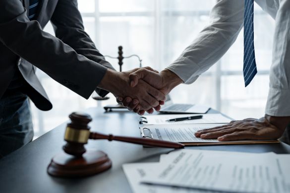 Two Men Are Shaking Hands Over a Table with A Gavel in The Background — Linda Emery & Associates In Morisset, NSW