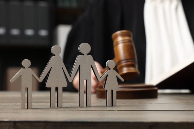 A Judge Is Sitting at A Table with A Wooden Gavel and Paper Cut Outs of A Family — Linda Emery & Associates In Bateau Bay, NSW