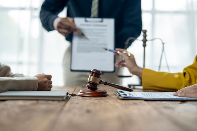 A Judge Is Holding a Piece of Paper in Front of A Couple of People Sitting at A Table — Linda Emery & Associates In Morisset, NSW