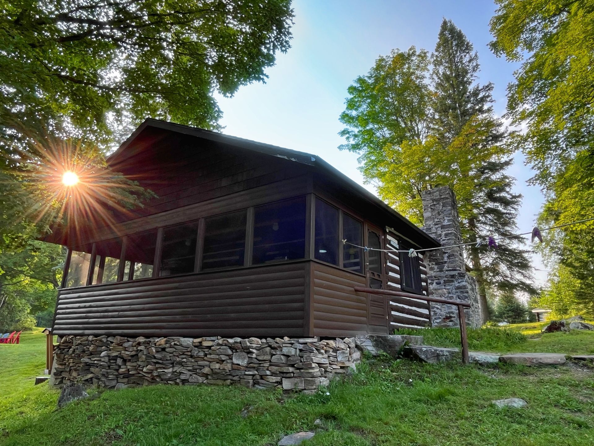 A log cabin in the middle of a forest with the sun shining through the trees