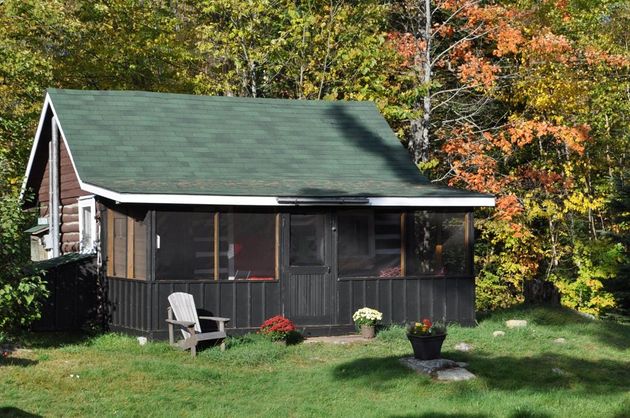 A log cabin with a screened in porch and chairs