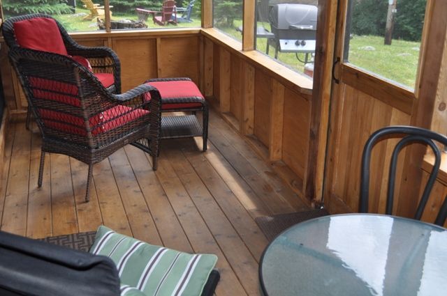 A screened in porch with wicker furniture and a glass table