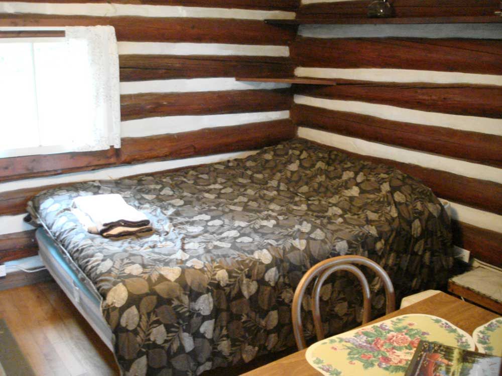 A bed in a log cabin next to a table and chairs