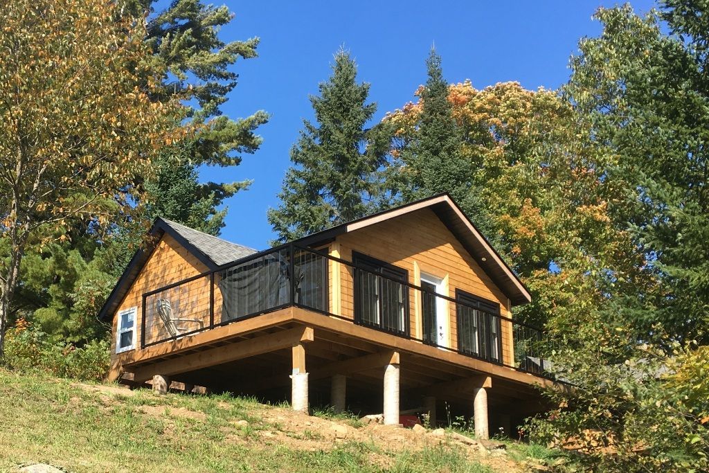 A small house with a large deck is sitting on top of a hill surrounded by trees.