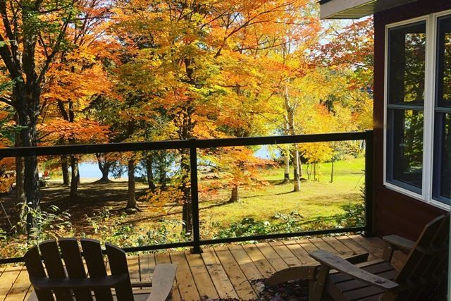 A deck with chairs and a view of trees and a lake.