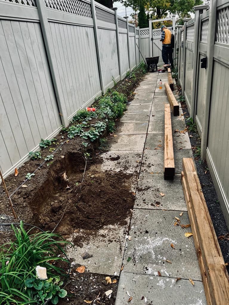 A narrow walkway with stone pavers, a flower bed being dug out, and a person working.