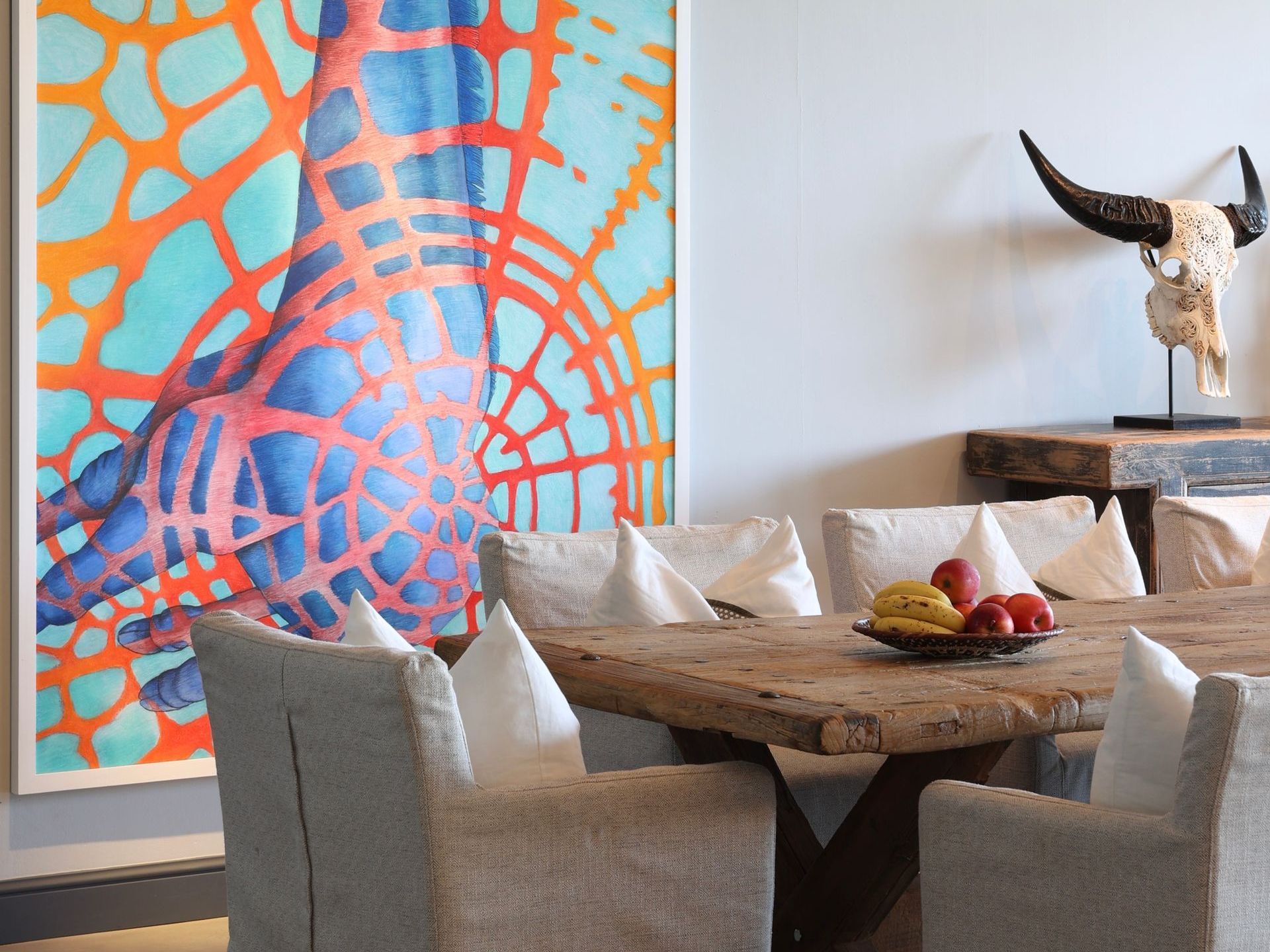 A dining room with a large painting on the wall above the table