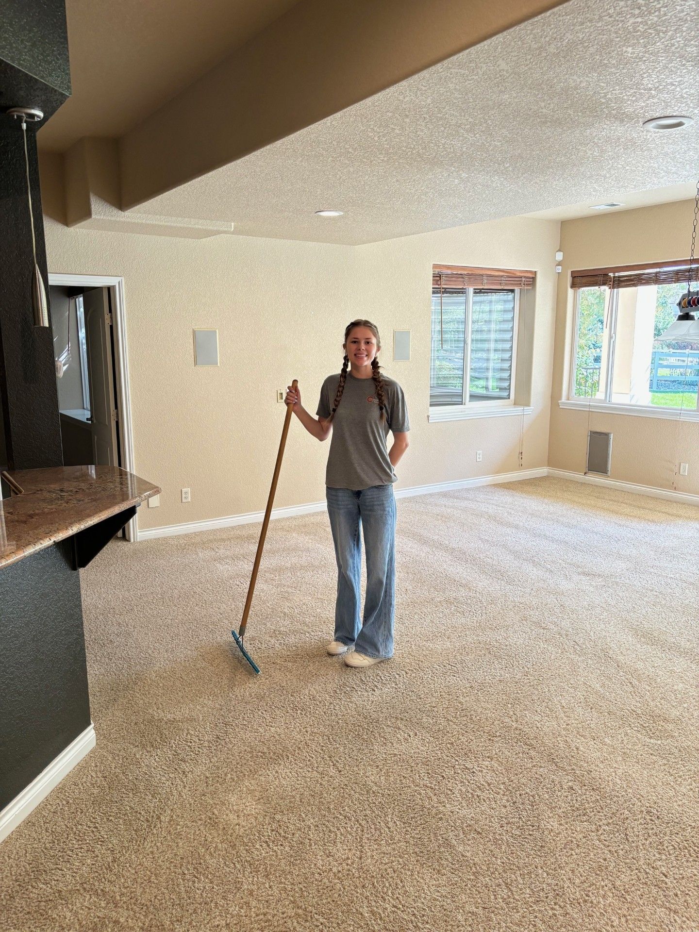 A woman is standing in an empty room holding a broom.
