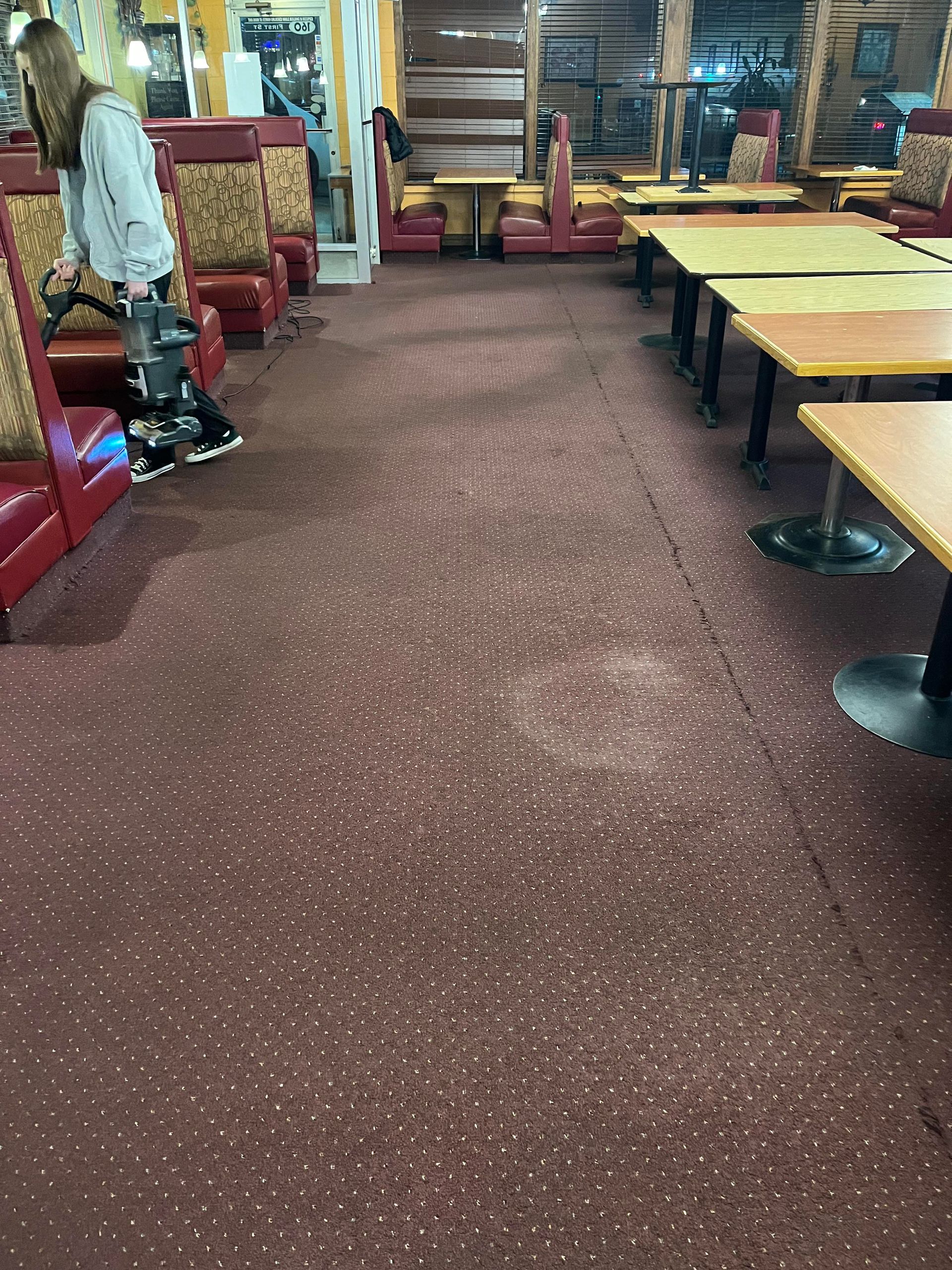 A woman is cleaning the floor of a diner with a vacuum cleaner