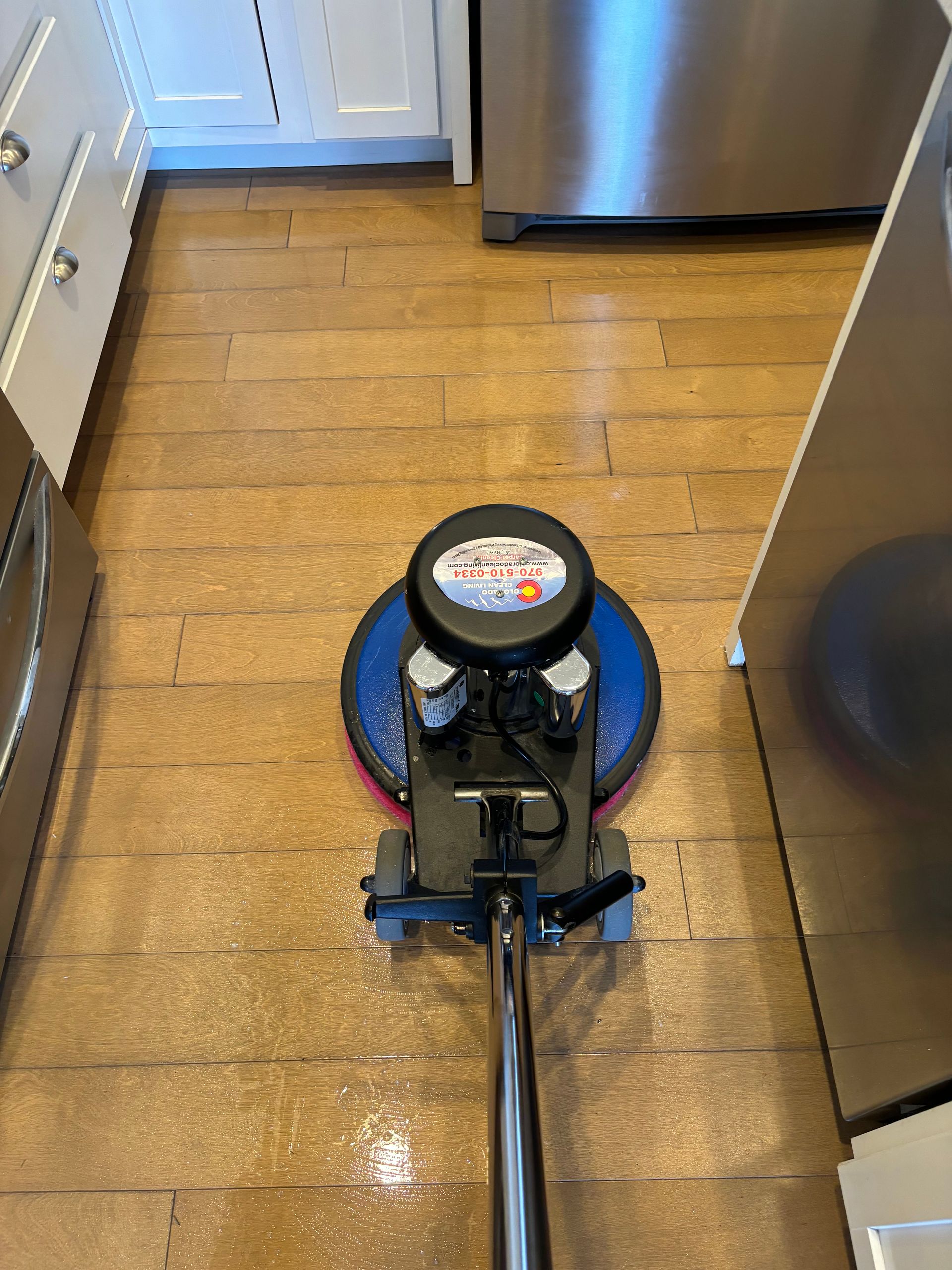 A machine is cleaning a wooden floor in a kitchen.