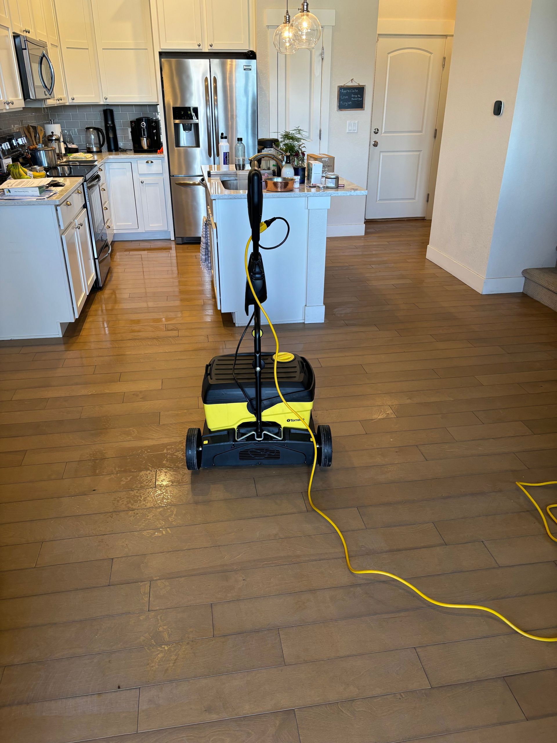 A vacuum cleaner is sitting on a wooden floor in a kitchen.