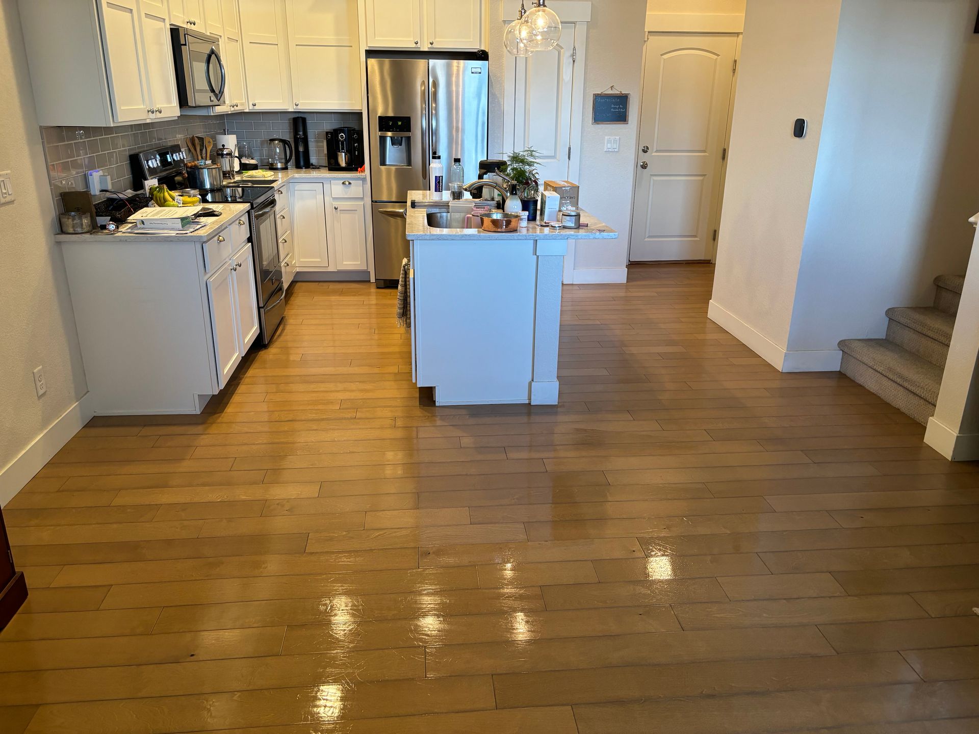 A kitchen with hardwood floors and white cabinets and stainless steel appliances.