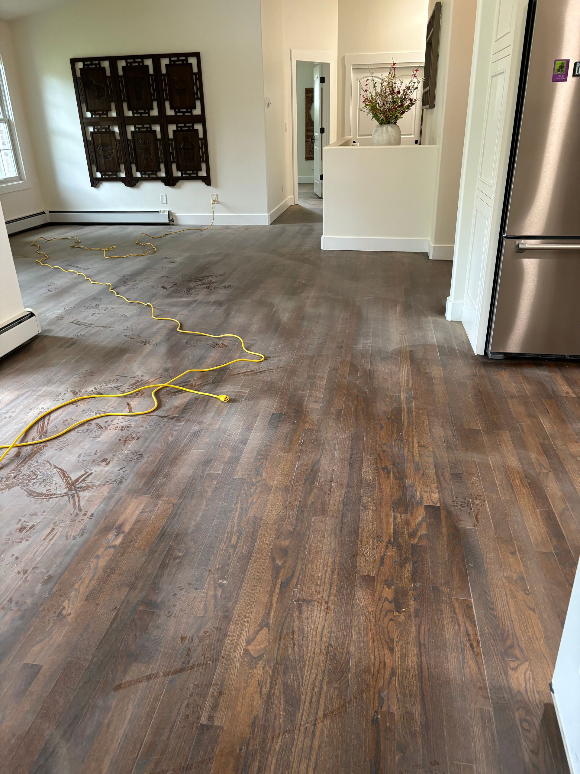 A living room with a wooden floor and a stainless steel refrigerator.