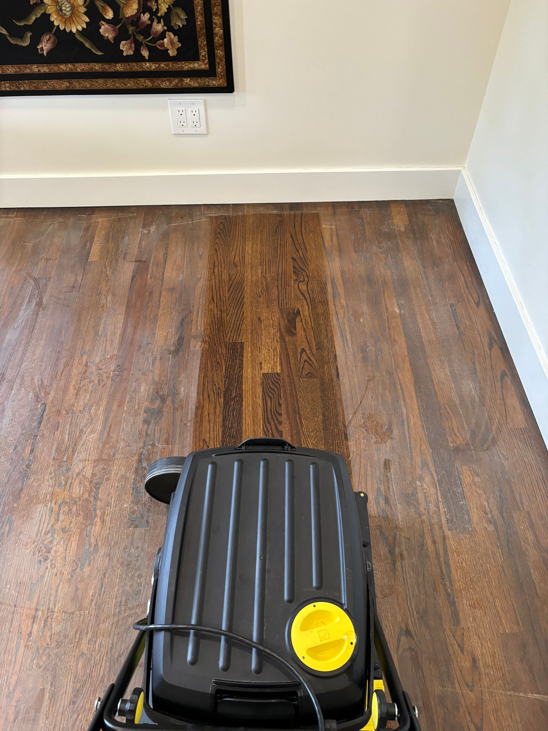 A vacuum cleaner is cleaning a wooden floor in a living room.