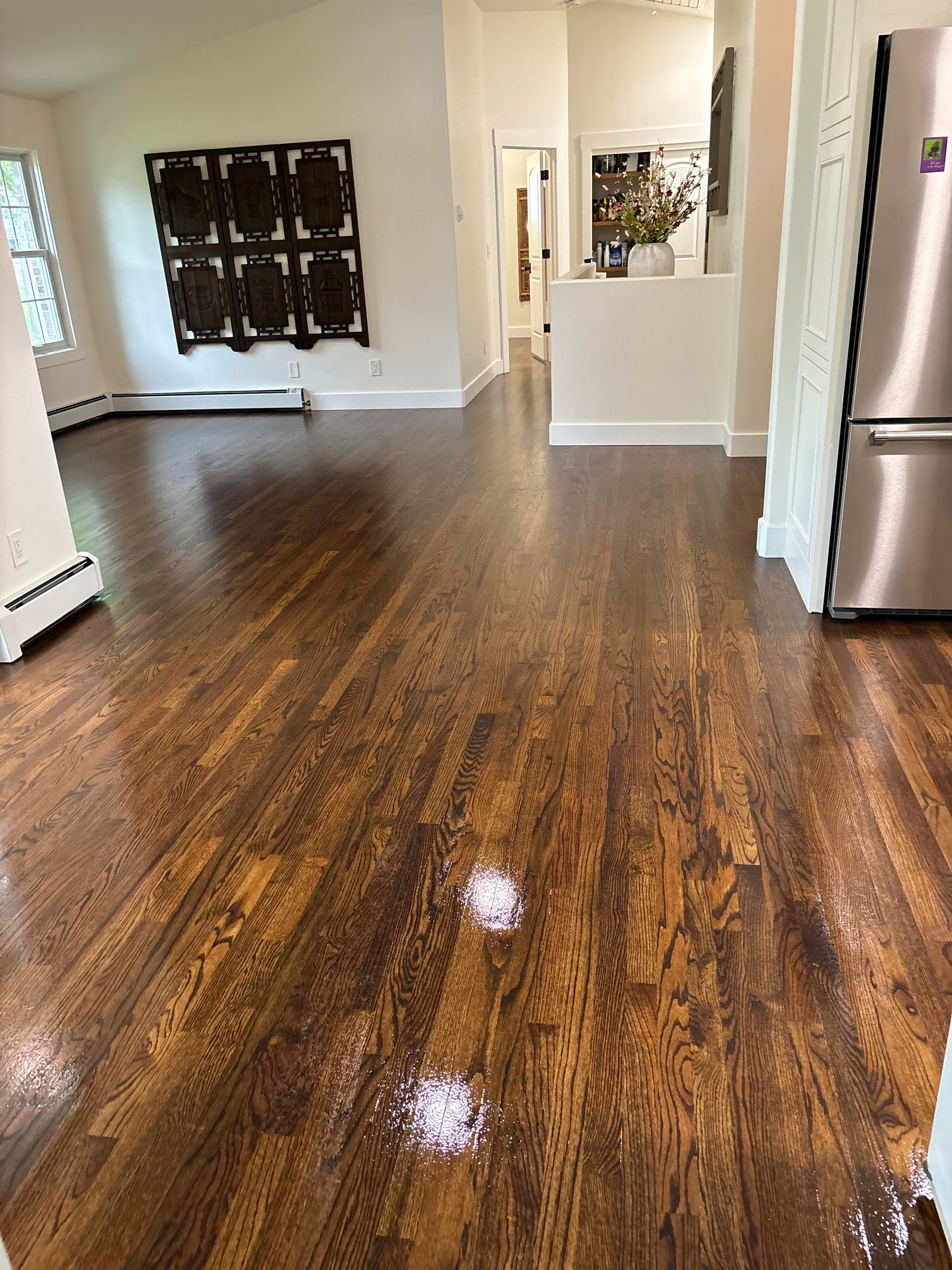 A living room with hardwood floors and a stainless steel refrigerator.