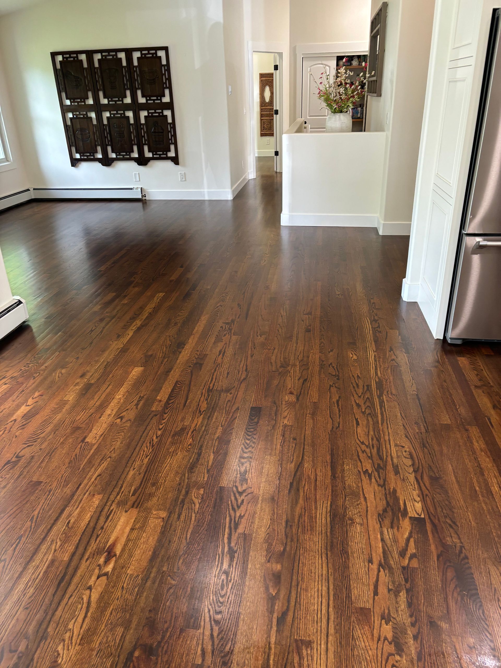 A living room with hardwood floors and a stainless steel refrigerator.